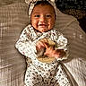 baby, child, infant, smiling, happy, portrait, lying_down, bed, bedroom, pajamas, onesie, headband, bow, hello_kitty, patterned_clothing, hands, feet, blanket, indoor, cute