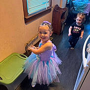 Lorelai joined the competition — help win amazing prizes! child, toddler, girl, dress, tutu, smile, indoor, floor, window, toy, party, headband, hair, clothing, person, furniture, table, chair, black_shirt, happy