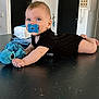 Aylonn participe au concours pour gagner de l'argent avec cette photo : baby, infant, pacifier, blue_pacifier, black_outfit, stuffed_toy, blue_toy, indoor, modern_room, table_surface, curious_expression, child, cute, lying_down, baby_toy, light_skin, short_hair, face, hand, foot