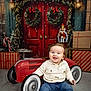 baby, toy_car, smiling, festive, christmas, wreath, presents, holiday, nutcracker, red_door, indoor, child, jeans, sweater, boots, floor, decorations, seasonal, happy, portrait