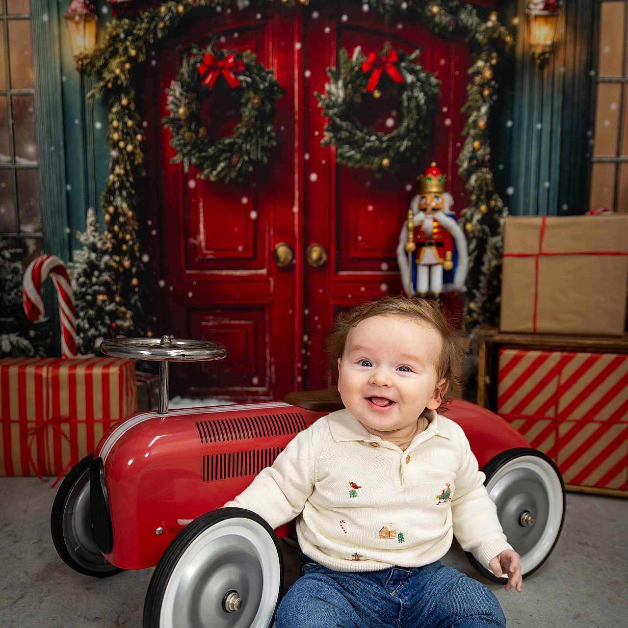 Hugh is registered to the contest to win money with this photo: baby, boots, child, christmas, decorations, festive, floor, happy, holiday, indoor, jeans, nutcracker, portrait, presents, red_door, seasonal, smiling, sweater, toy_car, wreath