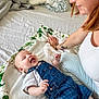 baby, bed, blanket, candid, casual_clothing, child, denim_overalls, glasses, happy, indoor, infant, joyful, light_skin, person, pillow, resting, smiling, tattoo, white_shirt, woman