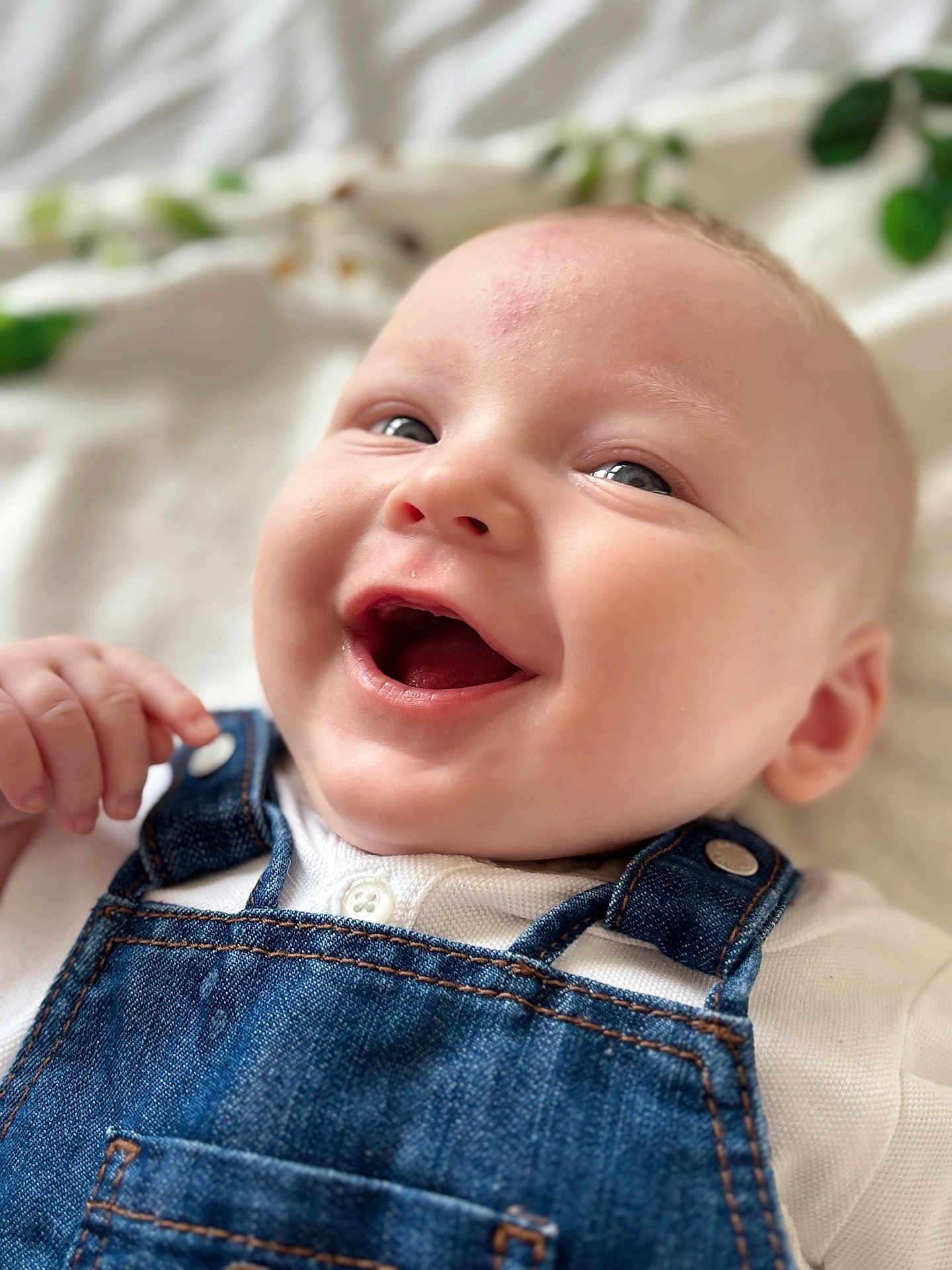 Timéo a rejoint le concours — aidez-le/la à gagner de superbes lots ! baby, smiling, denim_overalls, white_shirt, infant, closeup, face, happy, cute, child, skin, eyes, hand, portrait, young, fabric, button, casual_clothing, indoor, soft_light
