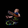 baby, barefoot, black_background, blue_clothing, bright_colors, child, curious_expression, face, goggles, helmet, infant, isolated, motocross, person, portrait, protective_gear, side_view, small_feet, sports_equipment, studio_shot