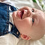 baby, background_blur, child, closeup, cute, denim_overalls, ear, eyes, face, happy, head, infant, lying_down, mouth, portrait, skin, smiling, soft_light, tongue_out, white_shirt