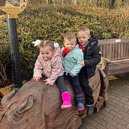 Lily Rose is registered to the contest to win money with this photo: child, children, outdoor, wooden_sculpture, rhino, bench, trees, jackets, boots, pacifier, play, park, winter_clothing, nature, smile, group, daylight, pavement, foliage, fun