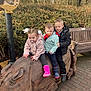 child, children, outdoor, wooden_sculpture, rhino, bench, trees, jackets, boots, pacifier, play, park, winter_clothing, nature, smile, group, daylight, pavement, foliage, fun