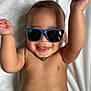 baby, child, sunglasses, mickey_mouse, tongue, smile, arms_up, gold_chain, bare_chest, playful, happy, infant, cute, portrait, lying_down, white_blanket, skin, person, close_up, fun