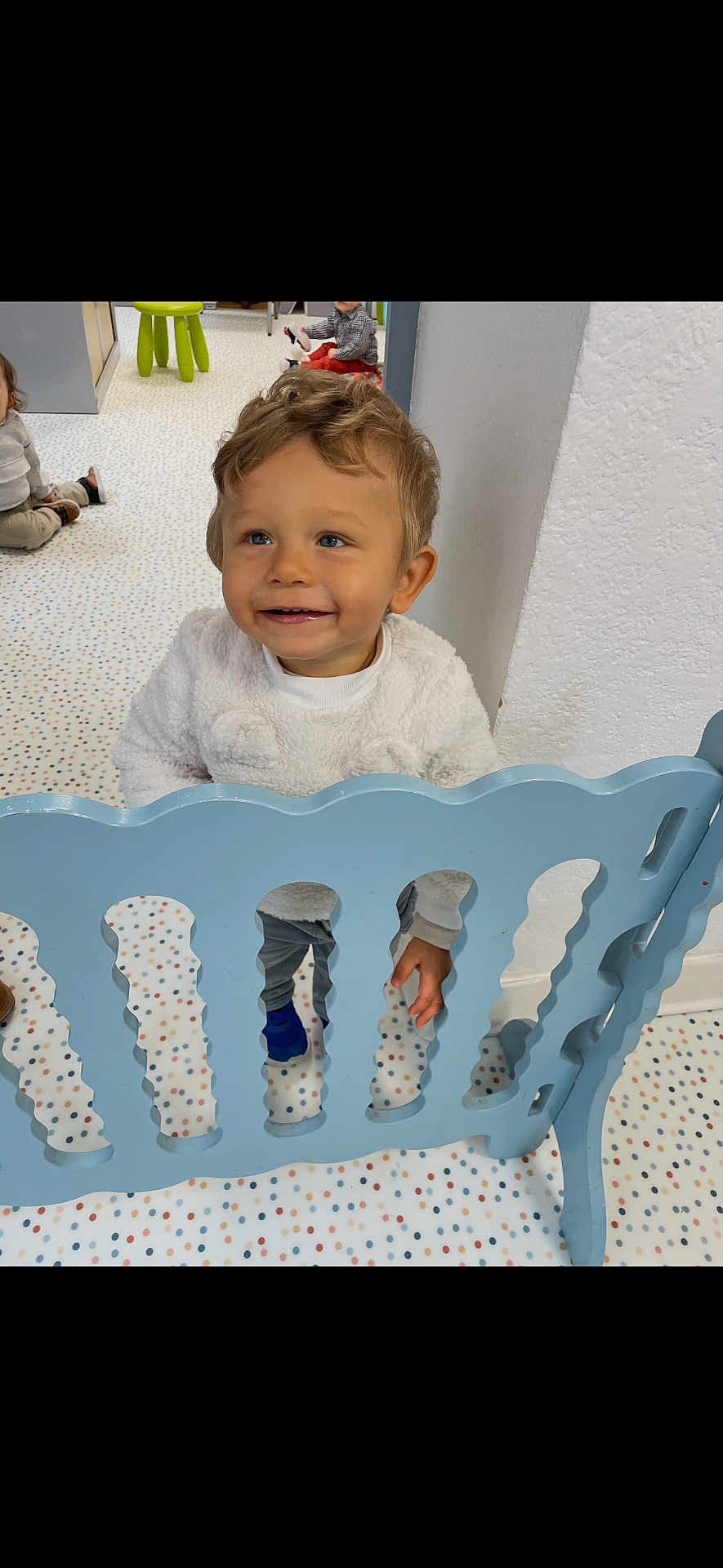 Lygan a rejoint le concours — aidez-le/la à gagner de superbes lots ! background_child, blue_gate, child, clothing, daycare, eyes, face, furniture, hair, hand, happy, indoor, playpen, playroom, polka_dot_floor, shoe, smile, standing, toddler, toy