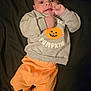 baby, infant, face, clothing, sweatshirt, pants, pumpkin, orange, gray, cute, lying_down, hand, expression, child, portrait, young, indoors, apparel, person, smiling