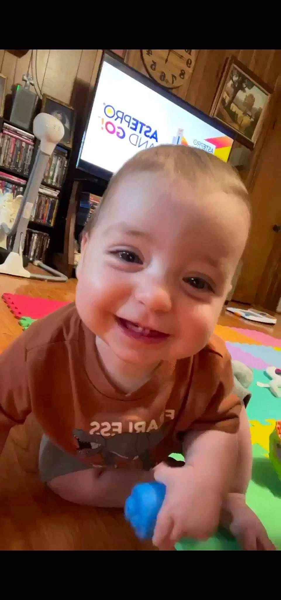 Anderson is registered to the contest to win money with this photo: baby, baby_toddler_clothing, bookcase, cheek, child, ear, eyelash, finger, flooring, fun, happy, iris, joy, mouth, nose, person, shelf, skin, smile, snapshot