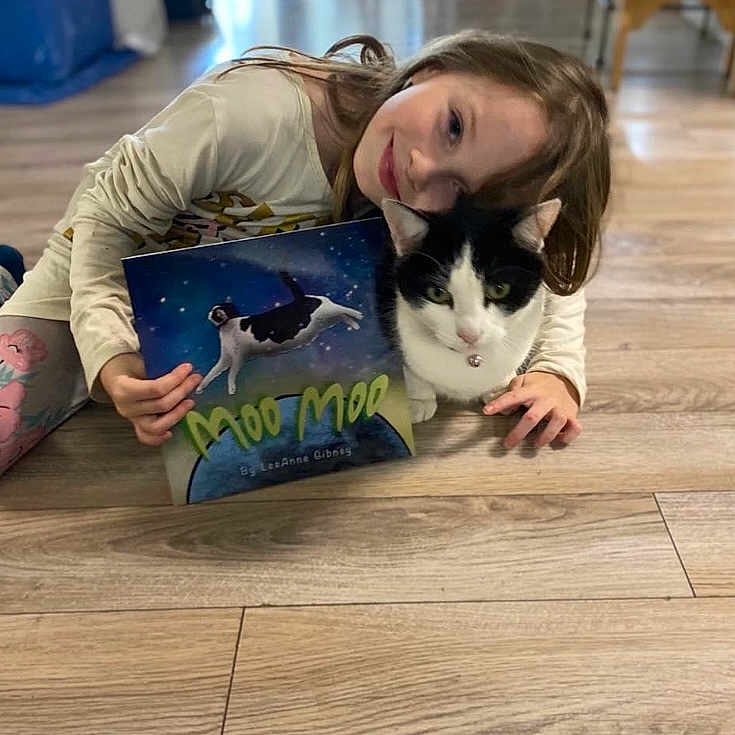 Moo Moo is registered to the contest to win money with this photo: carnivore, cat, child, domestic_short_haired_cat, felidae, flooring, fur, happy, hardwood, lap, leisure, publication, reading, sitting, small_to_medium_sized_cats, tail, thigh, whiskers, wood, wood_stain