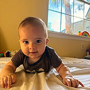 Kaleo is registered to the contest to win money with this photo: baby, infant, child, portrait, smiling, curious, indoor, bedroom, bed, blanket, striped_shirt, window, stained_glass, sunlight, toy, rainbow, hands, sitting, home, photography