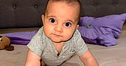 Kaleo is registered to the contest to win money with this photo: baby, infant, child, crawling, portrait, face, wide_eyes, indoor, bedroom, bed, pillow, purple_pillow, gray_shirt, short_sleeves, plush_toy, furniture, upholstery, home, photography, adorable