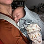 Nahil a rejoint le concours — aidez-le/la à gagner de superbes lots ! adult, baby, bonding, carrier, child, close_up, comfort, cozy, face, head, holding, indoor, onesie, pacifier, parent, patterned_clothing, person, resting, sleeping, soft_lighting