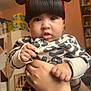 baby, child, red_bow, headband, leopard_print, clothing, hands, tattoos, bracelet, indoor, room, person, face, cute, curious, infant, holding, black_hair, portrait, expression