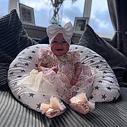 Havanna is registered to the contest to win money with this photo: baby, child, infant, dress, headband, bow, cushion, star_pattern, pillow, sofa, smile, indoors, window, vase, flowers, blurred_background, footwear, pink, happy, portrait