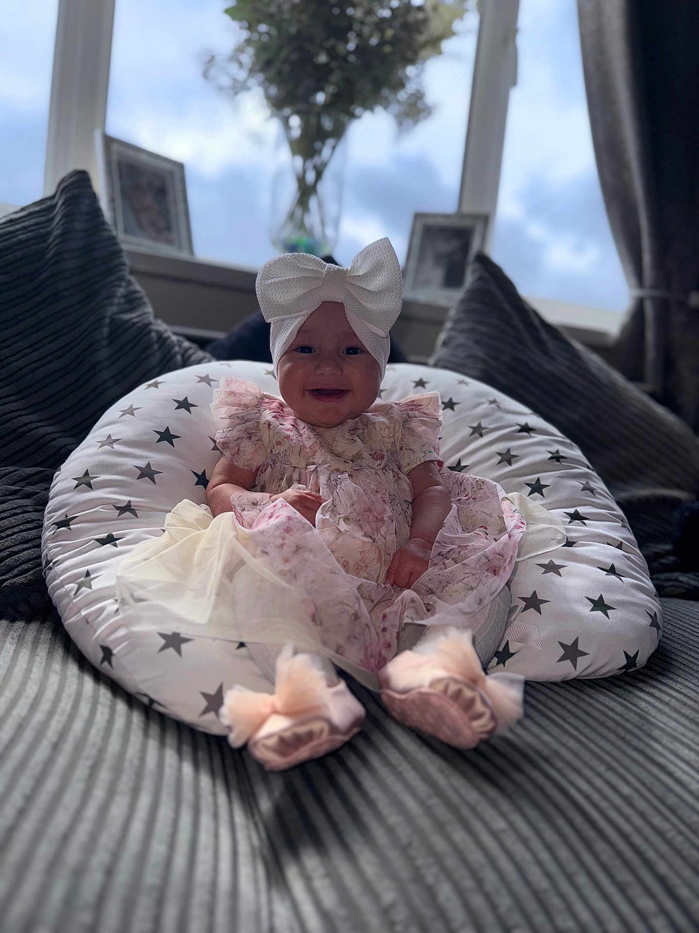 Havanna is registered to the contest to win money with this photo: baby, child, infant, dress, headband, bow, cushion, star_pattern, pillow, sofa, smile, indoors, window, vase, flowers, blurred_background, footwear, pink, happy, portrait