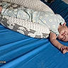 baby, child, infant, smiling, portrait, indoors, bed, mattress, pillow, blanket, sleeping, lying_down, floral_outfit, blue_bedding, barefoot, hand, face, happy, cozy, photograph