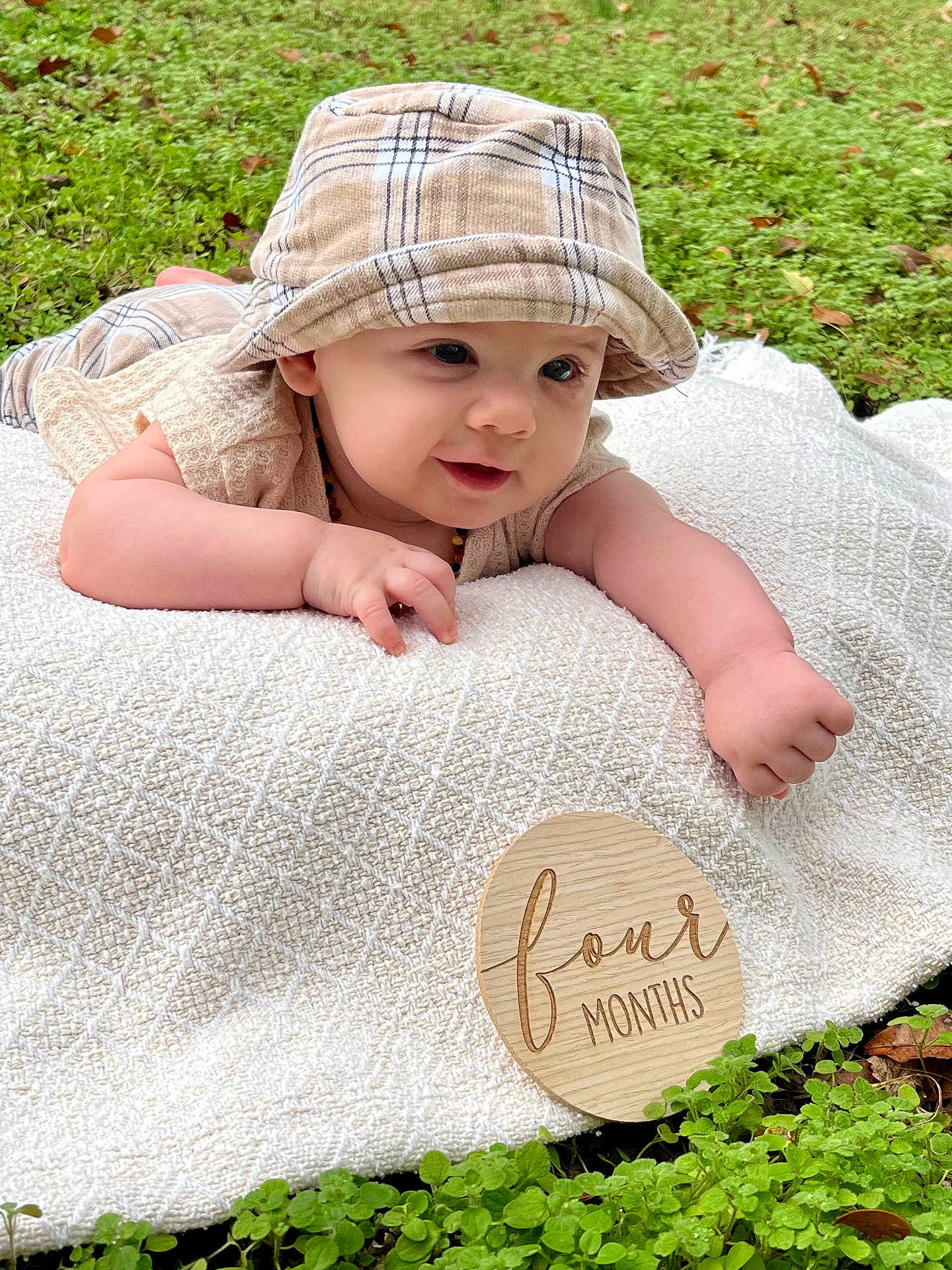 Copeland is registered to the contest to win money with this photo: baby, blanket, child, crawling, cute, four_months, grass, greenery, happy, hat, infant, nature, outdoor, person, plaid_hat, portrait, smiling, tummy_time, wooden_sign, young_child