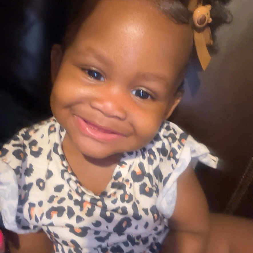Laiyani is registered to the contest to win money with this photo: baby, child, clothing, curly_hair, cute, face, hair_bow, happy, holding, indoor, leopard_print, person, playful, portrait, sitting, skin, smiling, toddler, toy, young_child