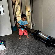 Andre Ariel is registered to the contest to win money with this photo: activity, blue_shirt, carpet, carpeted_floor, child, cleaning, coral_shorts, door, electrical_outlet, floor, footwear_absent, household, indoor, living_room, person, television, toy, toy_car, vacuum_cleaner, wall