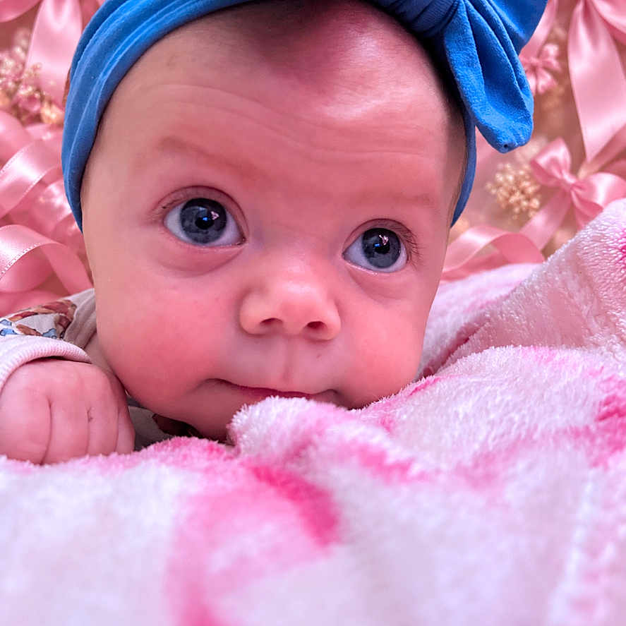 Brynlee Jade Walker joined the competition — help win amazing prizes! baby, infant, child, portrait, face, blue_bow, headband, pink_blanket, pink_background, wide_eyes, looking_at_camera, lying_down, cozy, soft_texture, nursery, indoor, close_up, adorable, fashion_accessory, photography