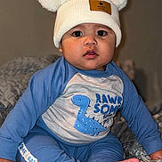 Dylan Nava joined the competition — help win amazing prizes! baby, child, hat, pom_poms, blue_clothing, dinosaur_graphic, sitting, blanket, indoors, cute, portrait, face, feet, hand, curious, wide_eyes, cozy, soft_lighting, infant, toddler