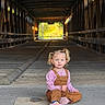 child, girl, toddler, portrait, sitting, wooden_bridge, covered_bridge, outdoor, forest, sunlight, pigtails, pink_shirt, overalls, pink_shoes, road, wood, perspective, travel, photography, smiling
