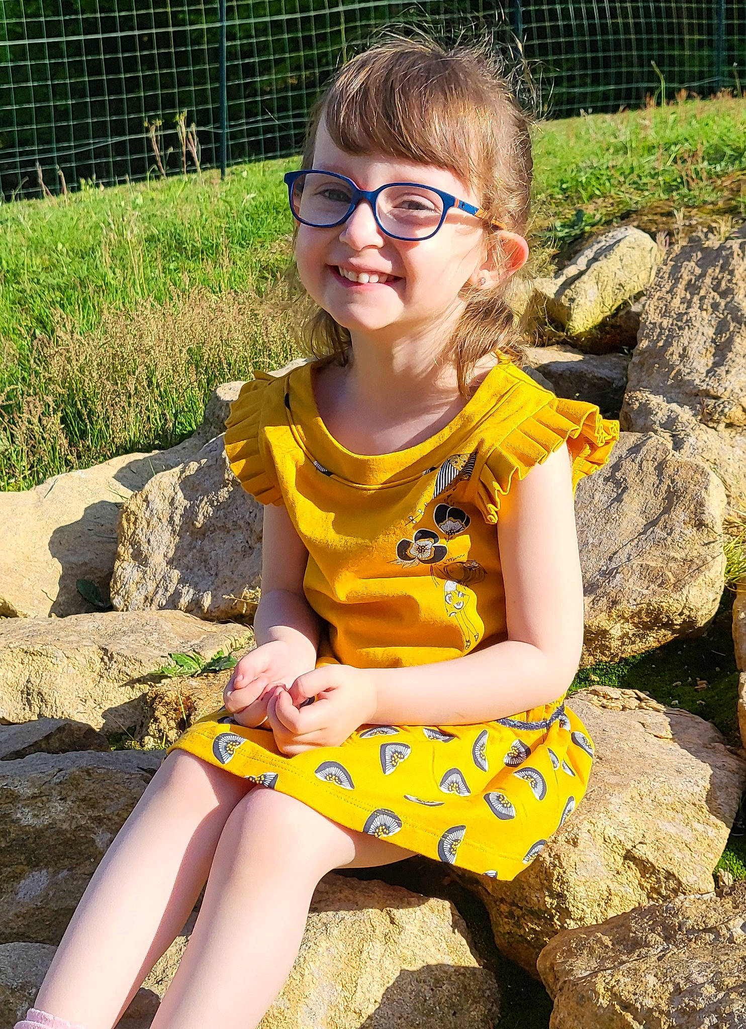 Alice participe au concours pour gagner de l'argent avec cette photo : blond, child, eye, eyewear, face, fence, finger, fun, glasses, grass, hairstyle, happy, human_leg, joy, leisure, people_in_nature, person, plant, smile, thigh