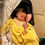 Makayla is registered to the contest to win money with this photo: baby, blanket, car_seat, child, cozy, doorway, face, floral_pattern, hair, hand, indoor, infant, onesie, pacifier, person, pink_trim, sleepy, soft_texture, toes, yellow_blanket