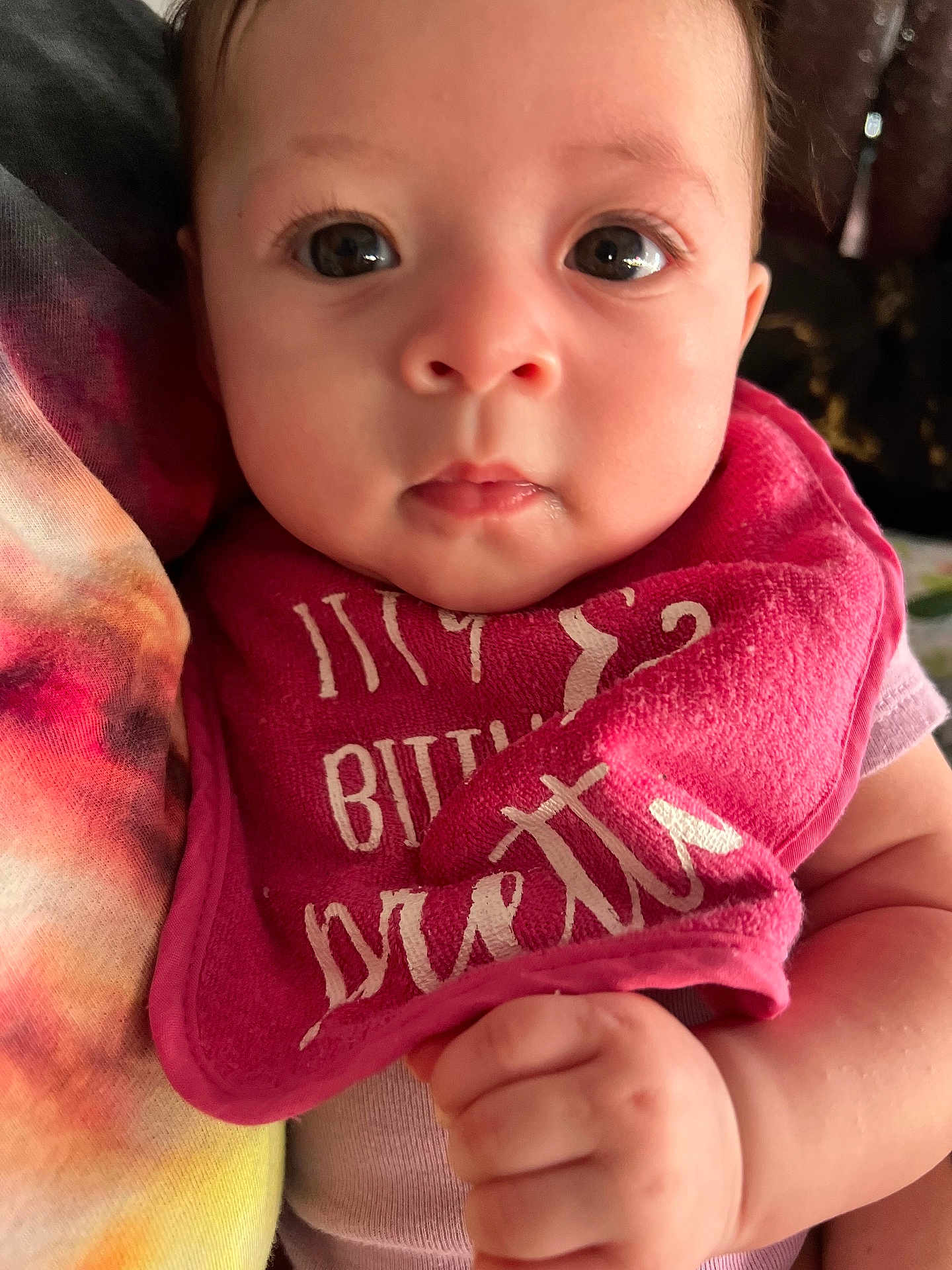 Makayla joined the competition — help win amazing prizes! baby, infant, close_up, face, eyes, pink_bib, hand, skin, curious, person, indoor, holding, child, portrait, young, cute, expression, clothing, soft_light, toddler