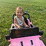 casual_clothing, child, cute, daylight, fun, grass, greenery, happy, nature, outdoor, person, pink, playtime, small_vehicle, smiling, summer, sunlight, toddler, toy_car, vehicle