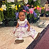 Harper is registered to the contest to win money with this photo: baby_shoes, carpet, child, cute, floral_dress, flowers, green_plants, happy, indoor, marble_floor, person, pink_flowers, portrait, purple_flower, purple_flowers, sitting, smiling, toddler, white_dress, yellow_tulips
