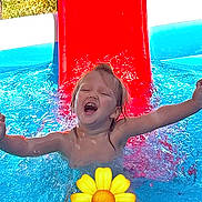 Lila is registered to the contest to win money with this photo: child, water, pool, slide, splash, happy, summer, outdoor, play, fun, yellow_flower_emoji, joy, swimming, arms_outstretched, daylight, wet_hair, blue_water, red_slide, person, smile