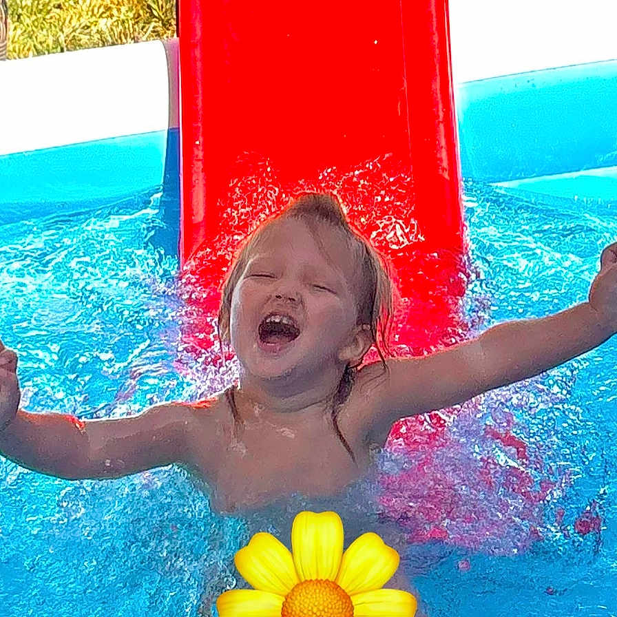 Lila is registered to the contest to win money with this photo: arms_outstretched, blue_water, child, daylight, fun, happy, joy, outdoor, person, play, pool, red_slide, slide, smile, splash, summer, swimming, water, wet_hair, yellow_flower_emoji