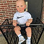 Louis is registered to the contest to win money with this photo: black_metal_cart, blue_eyes, brick_wall, casual_clothing, child, concrete_floor, cute, door, holding_cart_handle, nike_logo, outdoor, person, serious_expression, shopping_cart, short_hair, sign, sneakers, socks, toddler, white_shirt