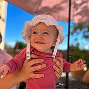 Amaya participe au concours pour gagner de l'argent avec cette photo : baby, child, white_hat, pink_outfit, smiling, hands, outdoor, umbrella, blue_sky, sunlight, happy, person, portrait, infant, cute, holding, summer, nature, table, daylight