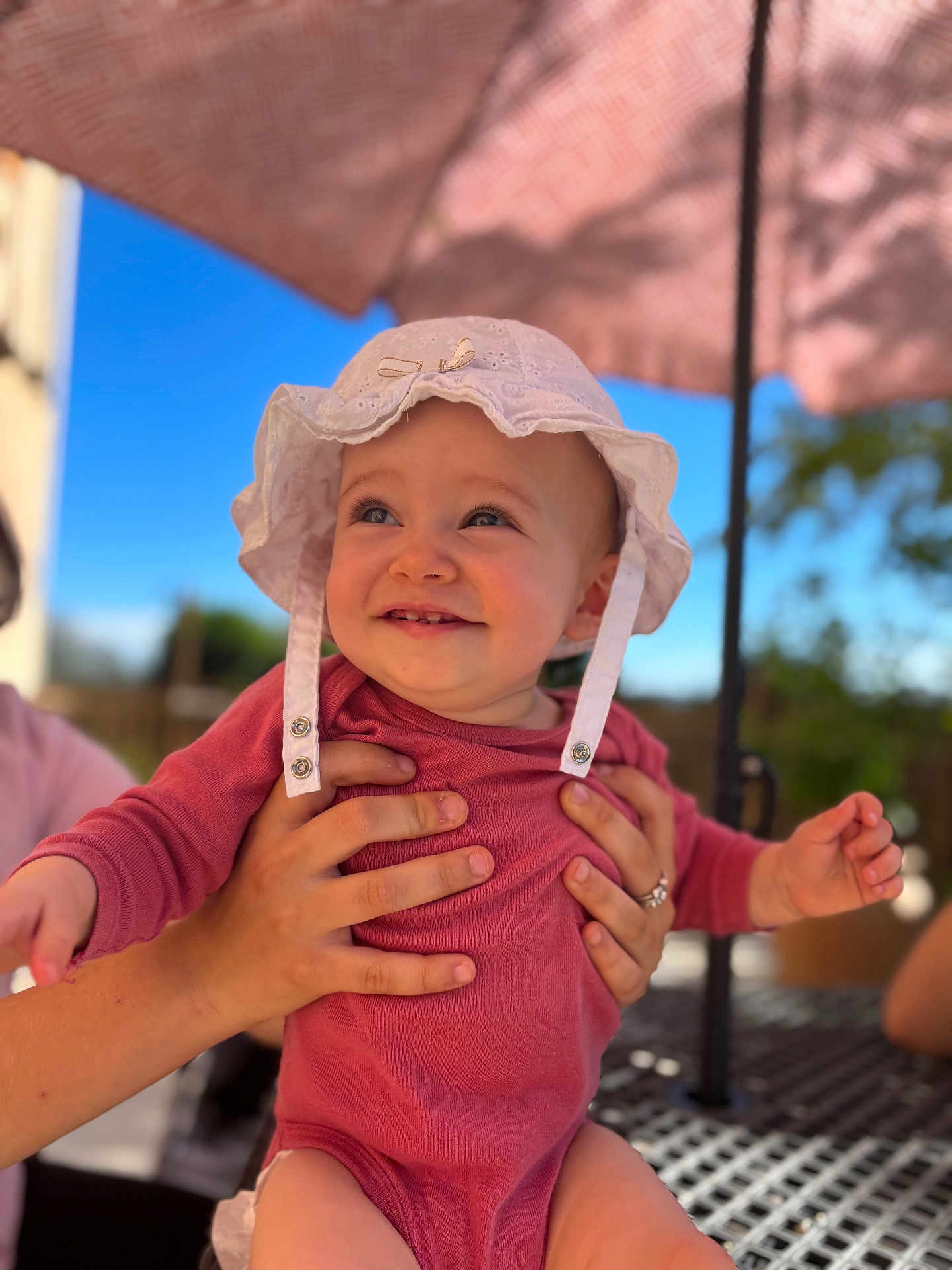 Amaya participe au concours pour gagner de l'argent avec cette photo : baby, child, white_hat, pink_outfit, smiling, hands, outdoor, umbrella, blue_sky, sunlight, happy, person, portrait, infant, cute, holding, summer, nature, table, daylight