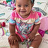 baby, child, smiling, portrait, sitting, indoor, play_mat, unicorn, toy, headband, flower, curly_hair, pink_clothing, rainbow, onesie, shoes, infant, happy, playroom, close_up