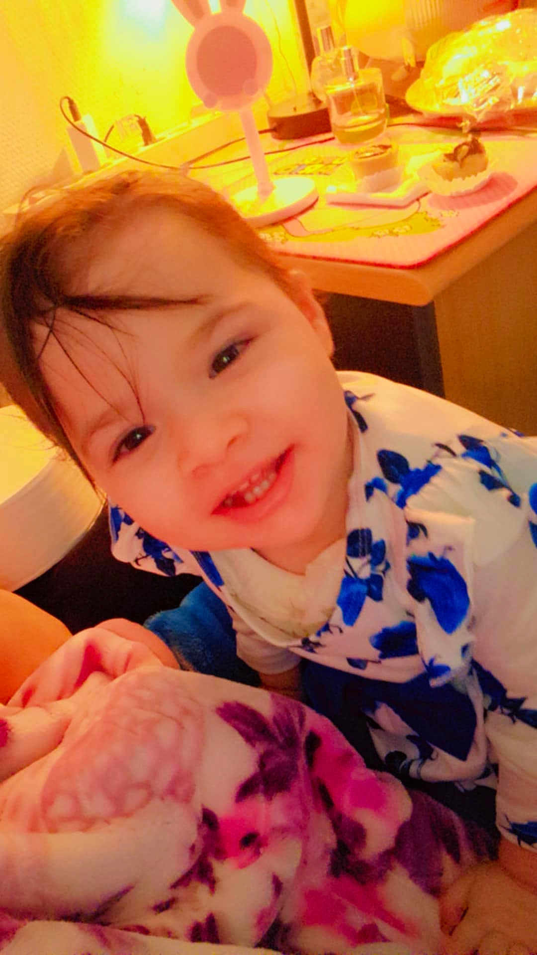 Dilara participe au concours pour gagner de l'argent avec cette photo : baby, blanket, bunny_lamp, child, clothing, cozy, cute, face, floral_pattern, food, happy, indoor, lamp, person, portrait, smiling, snack, table, toddler, warm_lighting