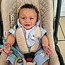 baby, child, car_seat, curly_hair, blue_clothing, adorable, smiling, bracelet, toy, indoor, seatbelt, happy, infant, person, cute, clothing, accessory, sitting, close_up, face