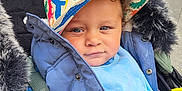 Syreese is registered to the contest to win money with this photo: toddler, child, hat, colorful, dinosaur_pattern, jacket, blue_clothing, stroller, baby, curly_hair, urban, outdoor, seatbelt, portrait, face, person, smile, casual, cute, warm_clothing