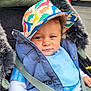 toddler, child, hat, colorful, dinosaur_pattern, jacket, blue_clothing, stroller, baby, curly_hair, urban, outdoor, seatbelt, portrait, face, person, smile, casual, cute, warm_clothing