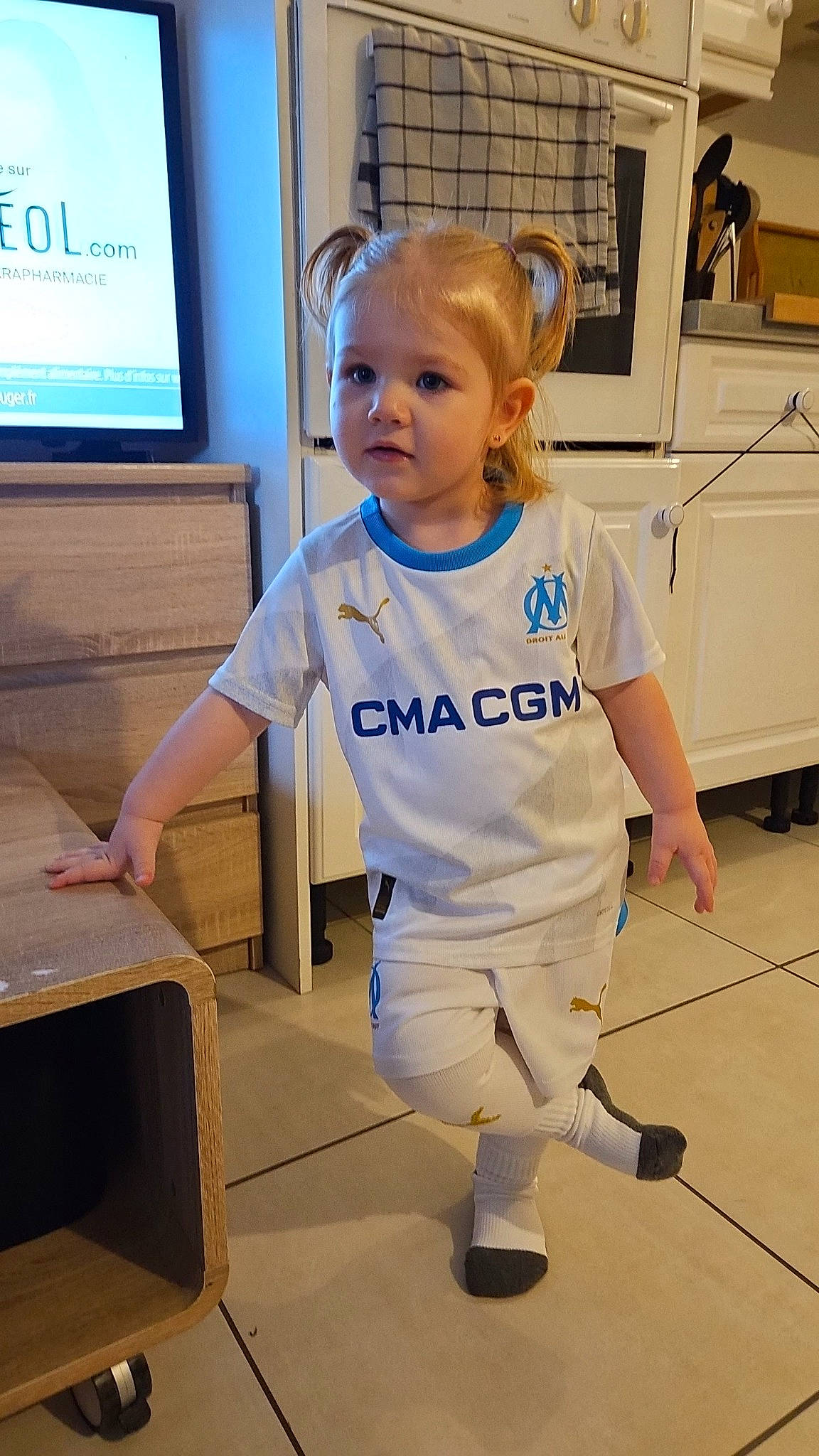 Alix a rejoint le concours — aidez-le/la à gagner de superbes lots ! baby_toddler_clothing, chair, child, electric_blue, flooring, fun, gesture, human_leg, joint, knee, person, room, shoulder, sleeve, sportswear, standing, sweatpant, t_shirt, television, thumb