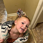 Hazel is registered to the contest to win money with this photo: child, smiling, blanket, bow, hair_accessory, indoor, floor, tile_floor, person, happy, cute, young_girl, earrings, home, wall, doorframe, playful, portrait, clothing, head