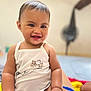 baby, child, smiling, happy, face, skin, hand, white_clothing, tank_top, sitting, indoors, blurred_background, cute, infant, portrait, young_child, person, short_hair, expression, human