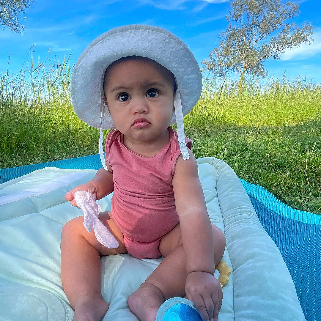 Teanivai participe au concours pour gagner de l'argent avec cette photo : baby, blue_sky, child, clouds, daylight, footwear, grass, hat, infant, mat, nature, outdoor, person, pink_onesie, portrait, serious_expression, sitting, sock, sunhat, toy
