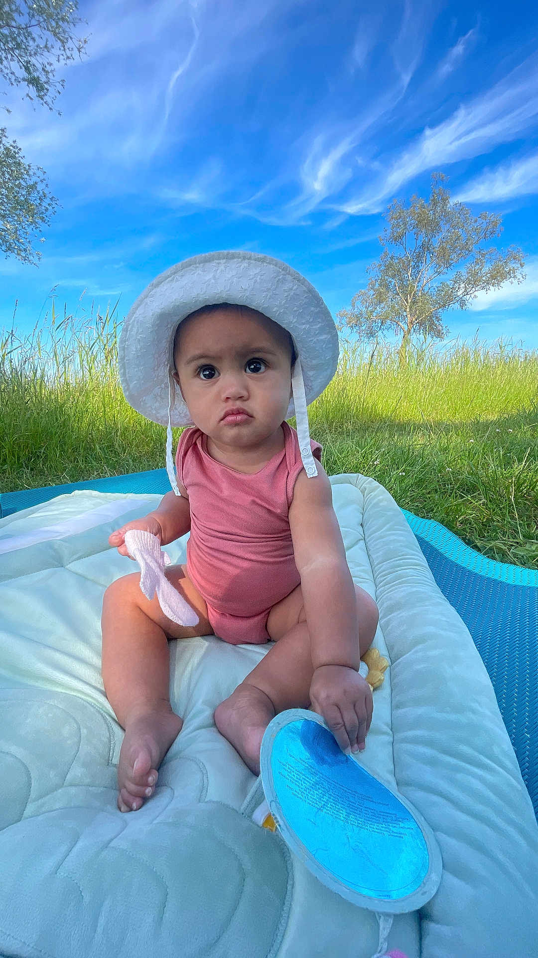 Teanivai participe au concours pour gagner de l'argent avec cette photo : baby, child, hat, sunhat, pink_onesie, outdoor, grass, blue_sky, clouds, mat, toy, sock, serious_expression, sitting, footwear, nature, daylight, infant, person, portrait