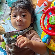 Samuel is registered to the contest to win money with this photo: baby, child, infant, toy, play_mat, colorful, soft_toy, lying_down, cute, indoors, clothing, hand, face, expression, young_child, playtime, comfort, background, closeup, portrait